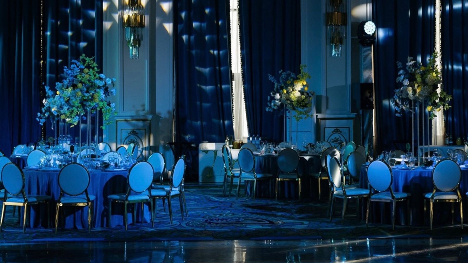 Зал Palazzo Di Astana вечером: круглые столы под синим, кресла в золочёных рамах, высокие цветочные композиции и зеркальный пол